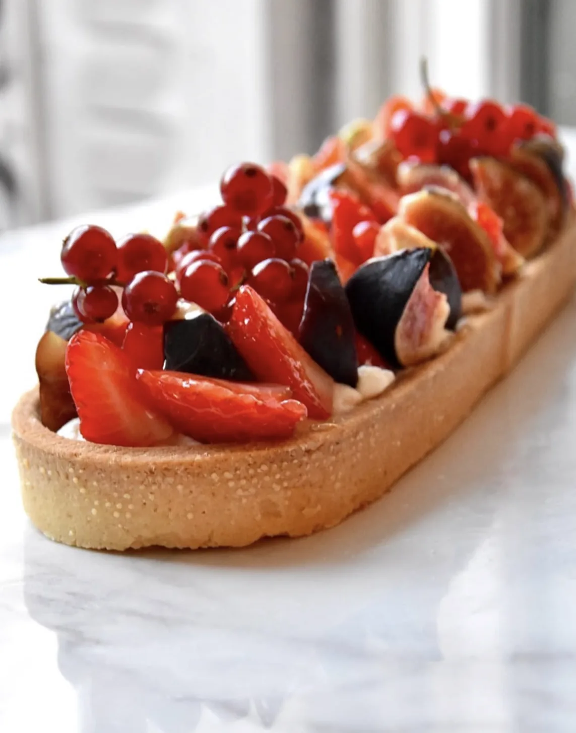 Une tarte longue aux fruits rouges et aux figues sur un plan de marbre