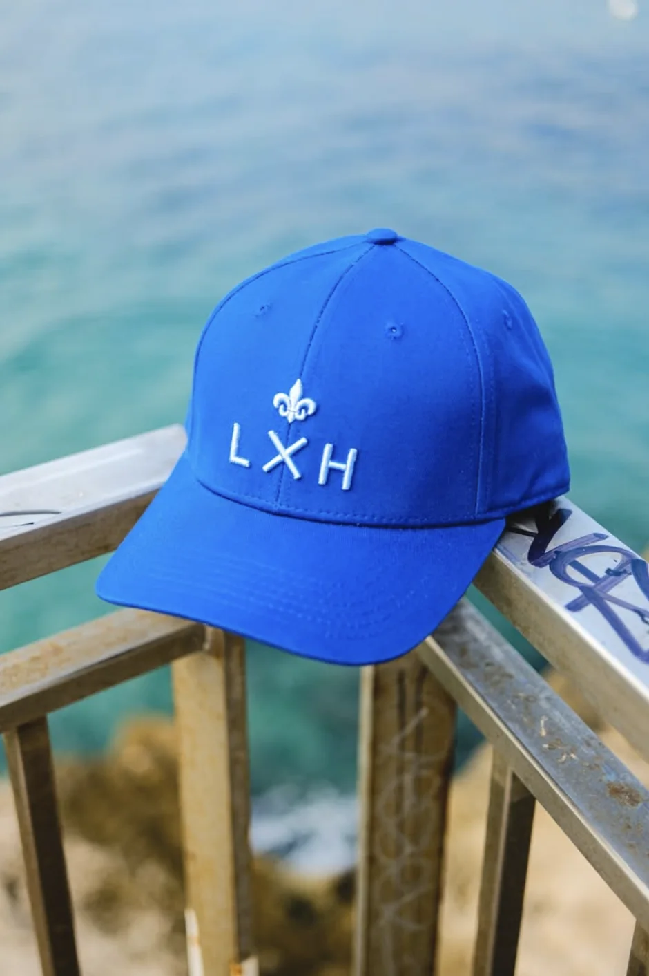 Une casquette LXH posée sur une rambarde, la mer en fond