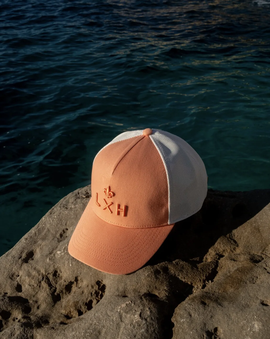 Une casquette LXH corail posée sur un rocher, bord de mer