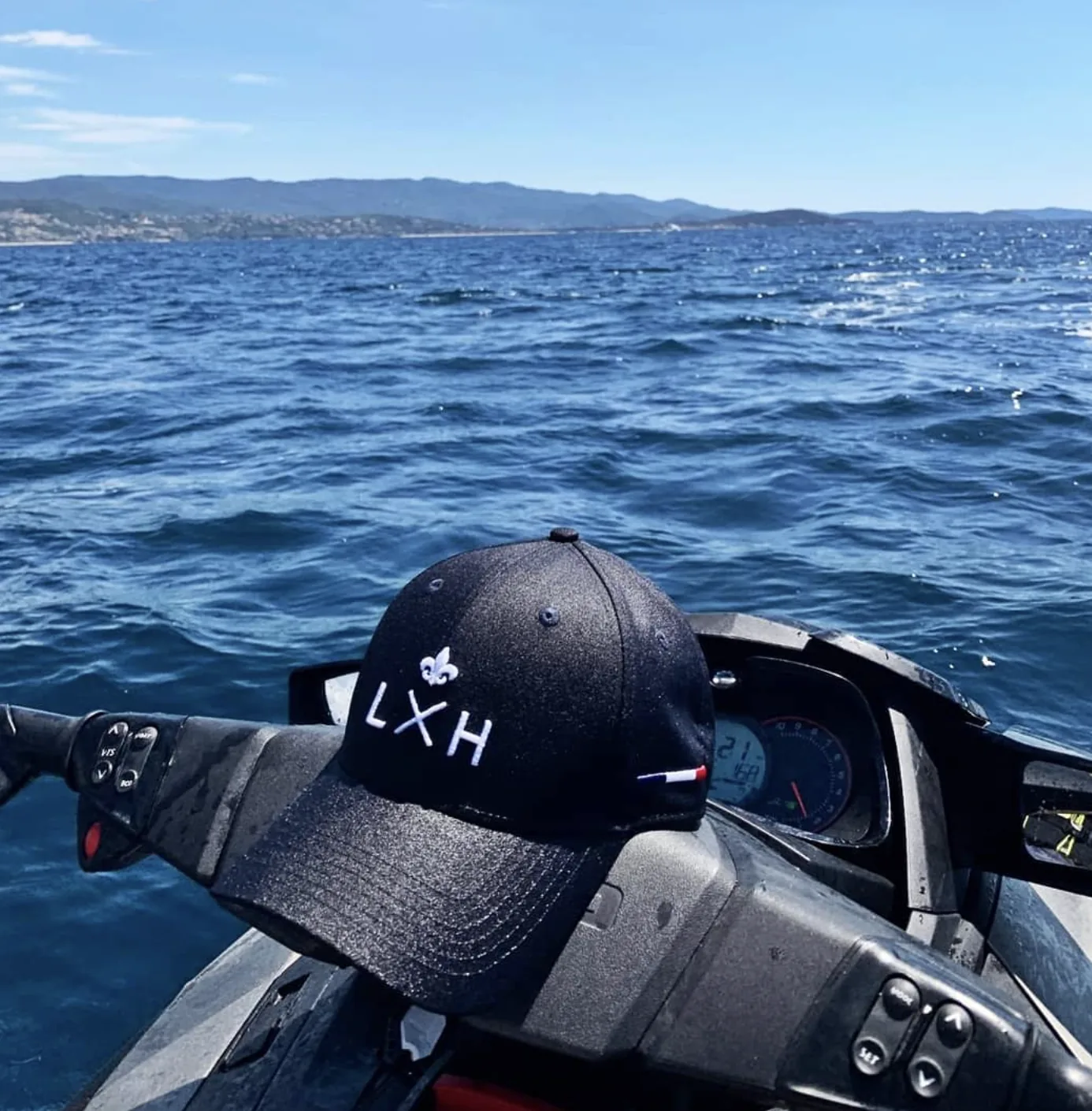 Une casquette LXH posée sur le guidon d'un jet ski, la mer au large